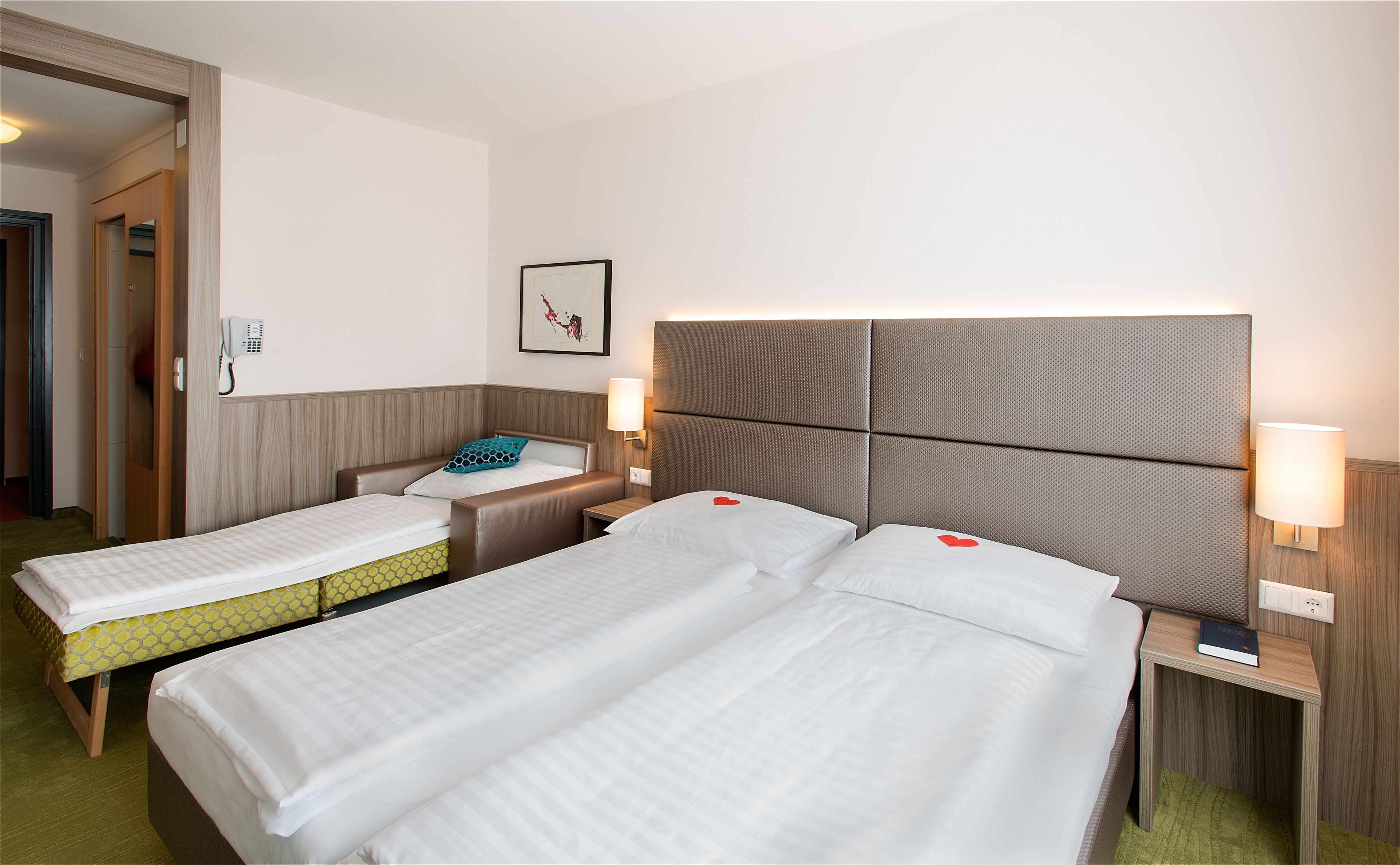Habitación de hotel con dos camas, una mesita de noche con lámpara, teléfono y un cuadro en la pared.