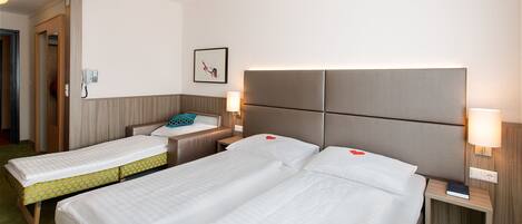 A hotel room with two beds, a bedside table with a lamp, a phone, and a framed picture on the wall.