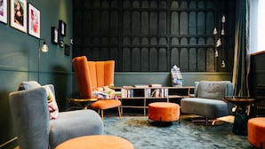 A modern living room with a dark wooden wall, a bookshelf, and orange and grey furniture. - Hotel City Villach (Villach)