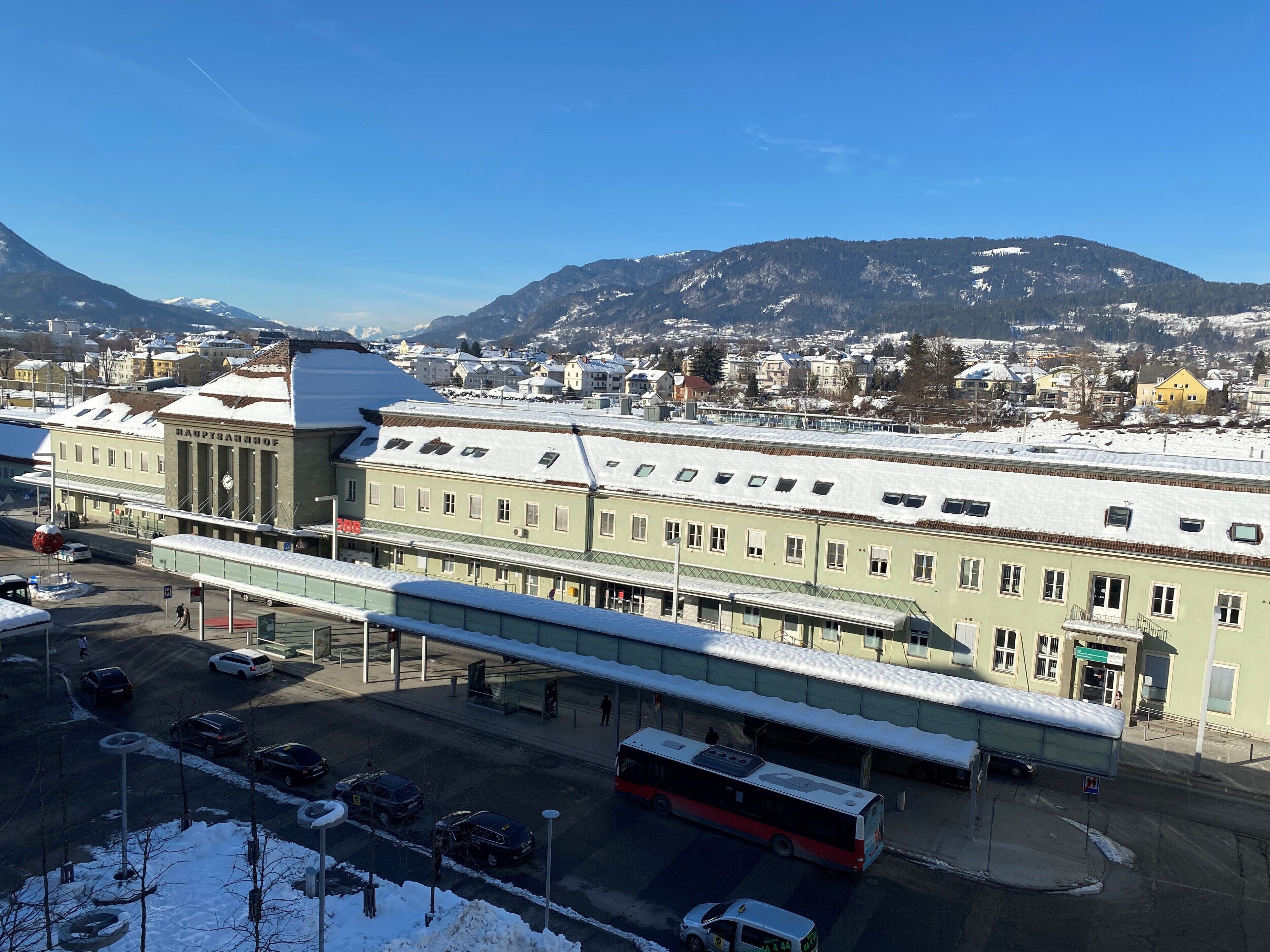 Un edificio con una entrada amplia, una estación de autobuses cubierta y una montaña nevada al fondo.