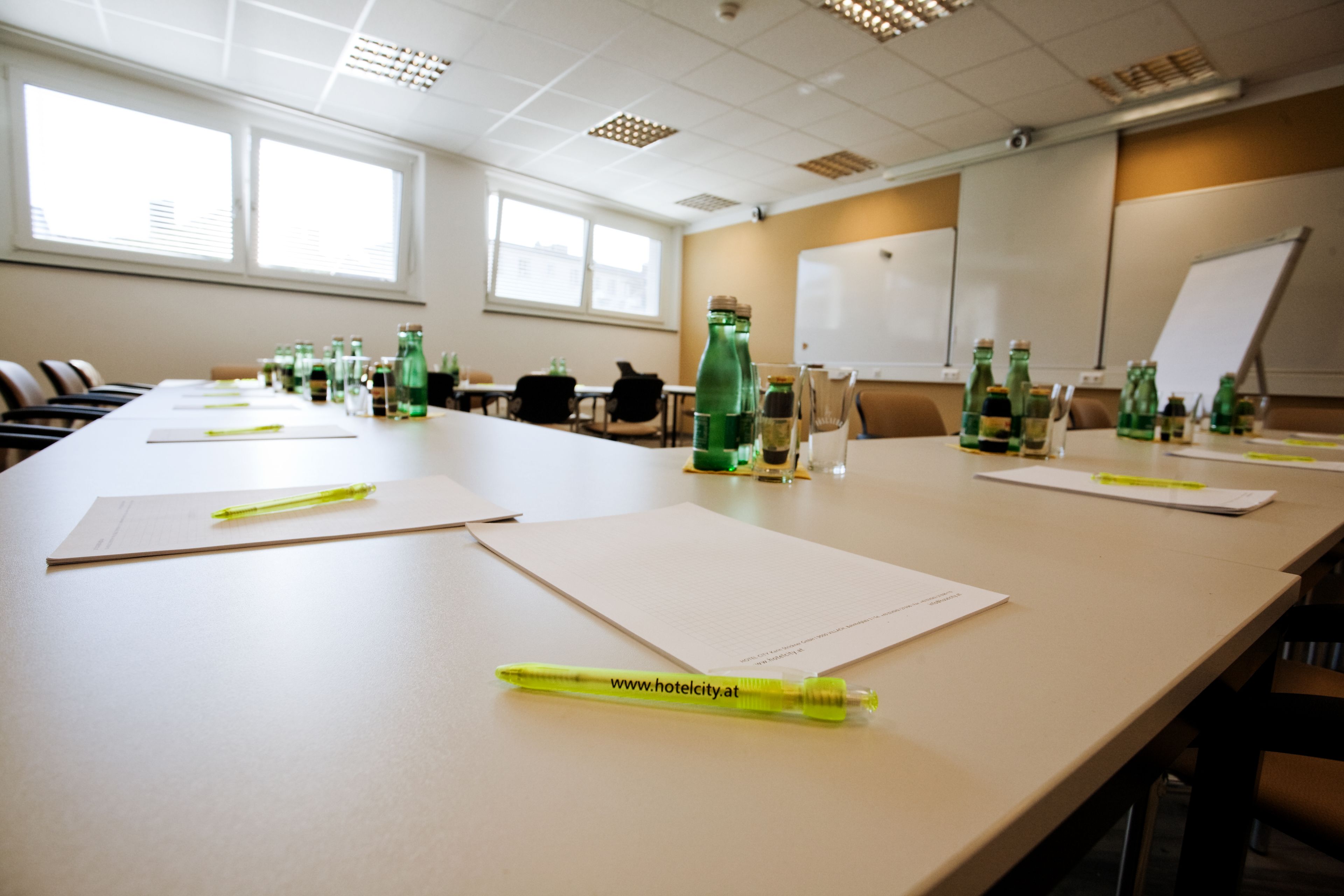 A conference room with a long table, chairs, a whiteboard, and green bottles.