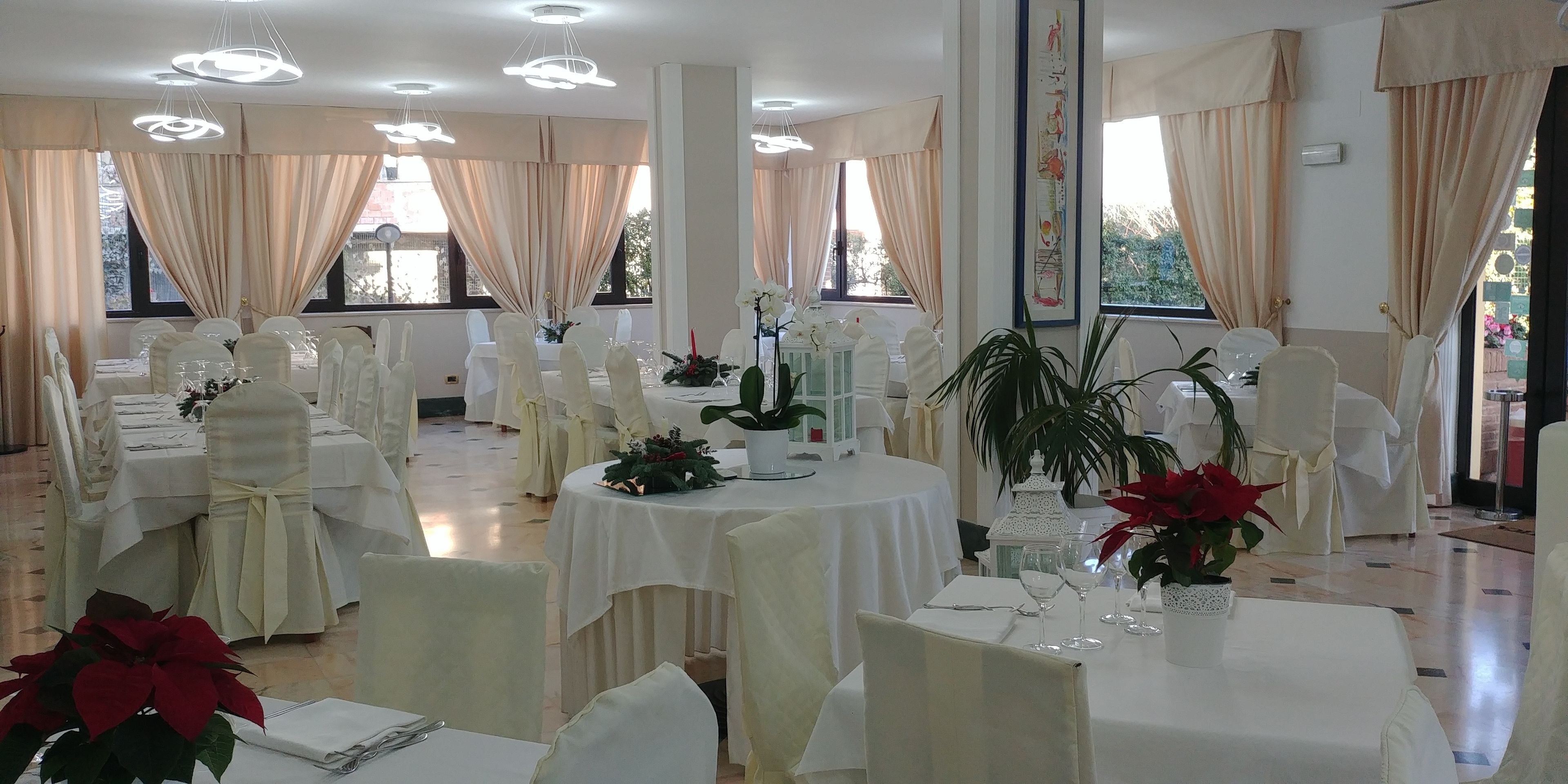 A banquet hall with round tables, white tablecloths, and chairs with white covers.