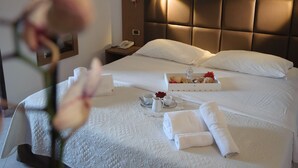 Una cama bien tendida con sábanas blancas, una mesita de noche con un teléfono y una bandeja con alimentos para el desayuno.