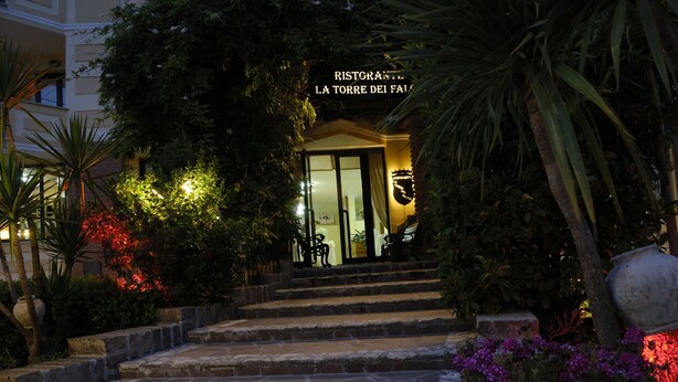 Entrada de un restaurante con escalones de piedra, rodeada de abundante vegetación e iluminada por luces cálidas.