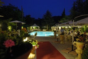 Zona de piscina al aire libre con mobiliario y sombrillas, rodeada de follaje.