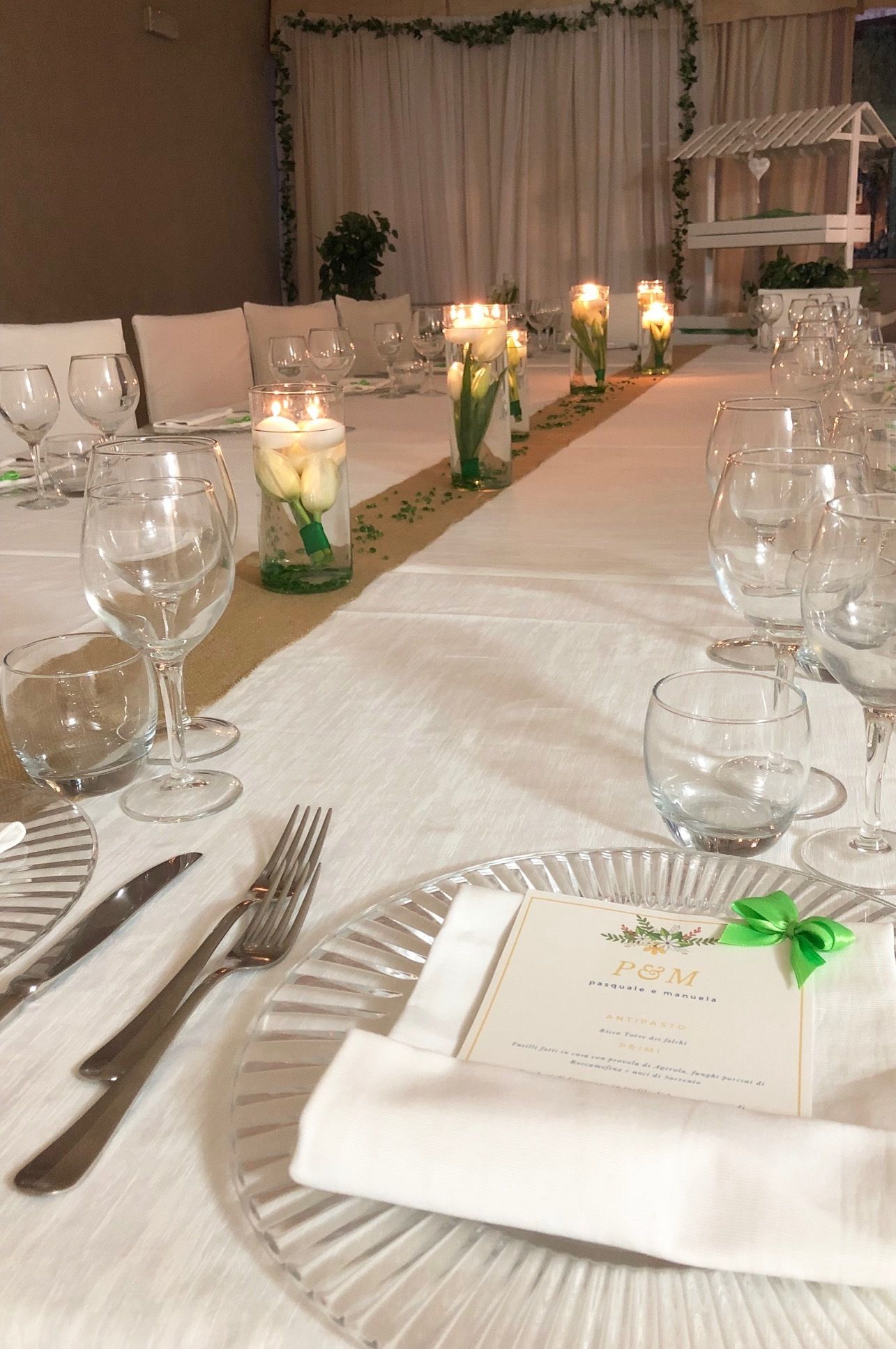 Una mesa de banquete dispuesta con manteles blancos, copas de cristal transparente y velas.