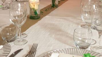 Una mesa de banquete dispuesta con manteles blancos, copas de cristal transparente y velas.