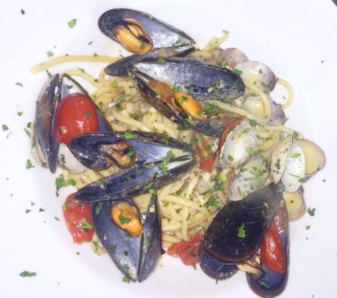 A plate of mussels with pasta and tomatoes, garnished with herbs.