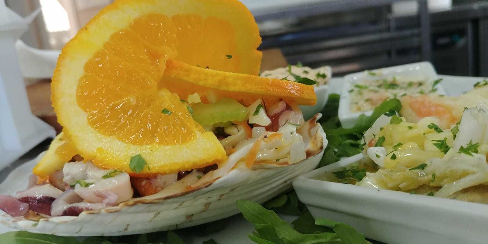 A seafood dish in a shell, garnished with an orange slice and herbs.