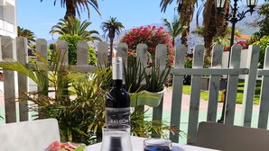 Una mesa para comer al aire libre con una botella de vino, una copa de vino tinto, una hogaza de pan, una ensalada y un plato de comida.