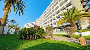 Un hotel de varios pisos con un diseño arquitectónico moderno, que cuenta con un patio central con palmeras y abundante vegetación.