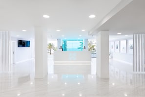 Una zona d'entrada moderna amb una paret de vidre, un taulell de recepció i una televisió penjada.