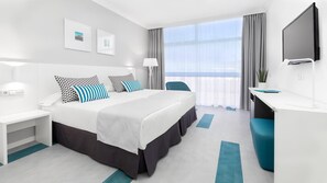 Habitació d'hotel amb llit, escriptori, cadira i una finestra gran amb cortines.