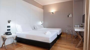 Habitación de hotel con dos camas, un escritorio con silla, un teléfono y una lámpara fijada a la pared.