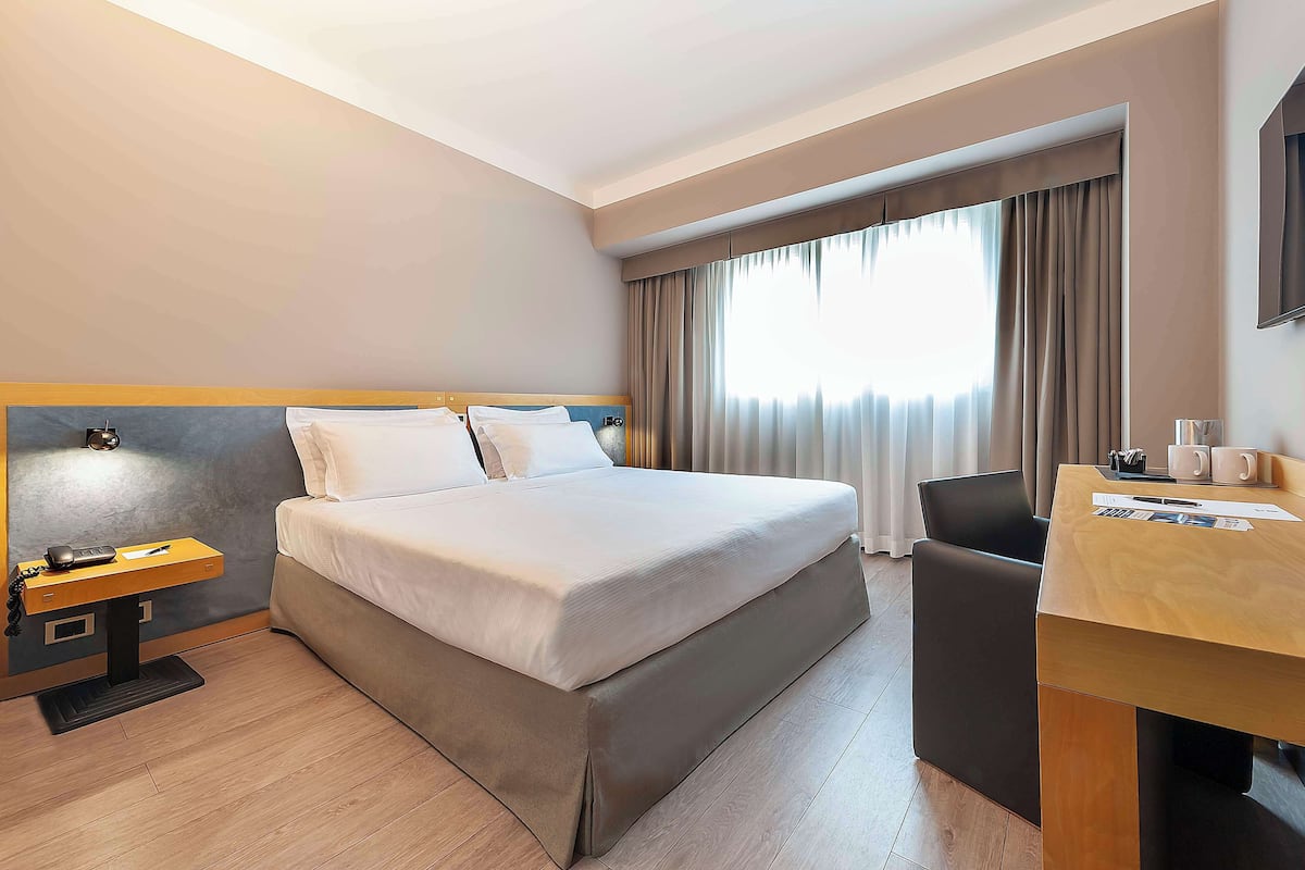 Une chambre d’hôtel avec un lit, un bureau, une chaise et un téléviseur.