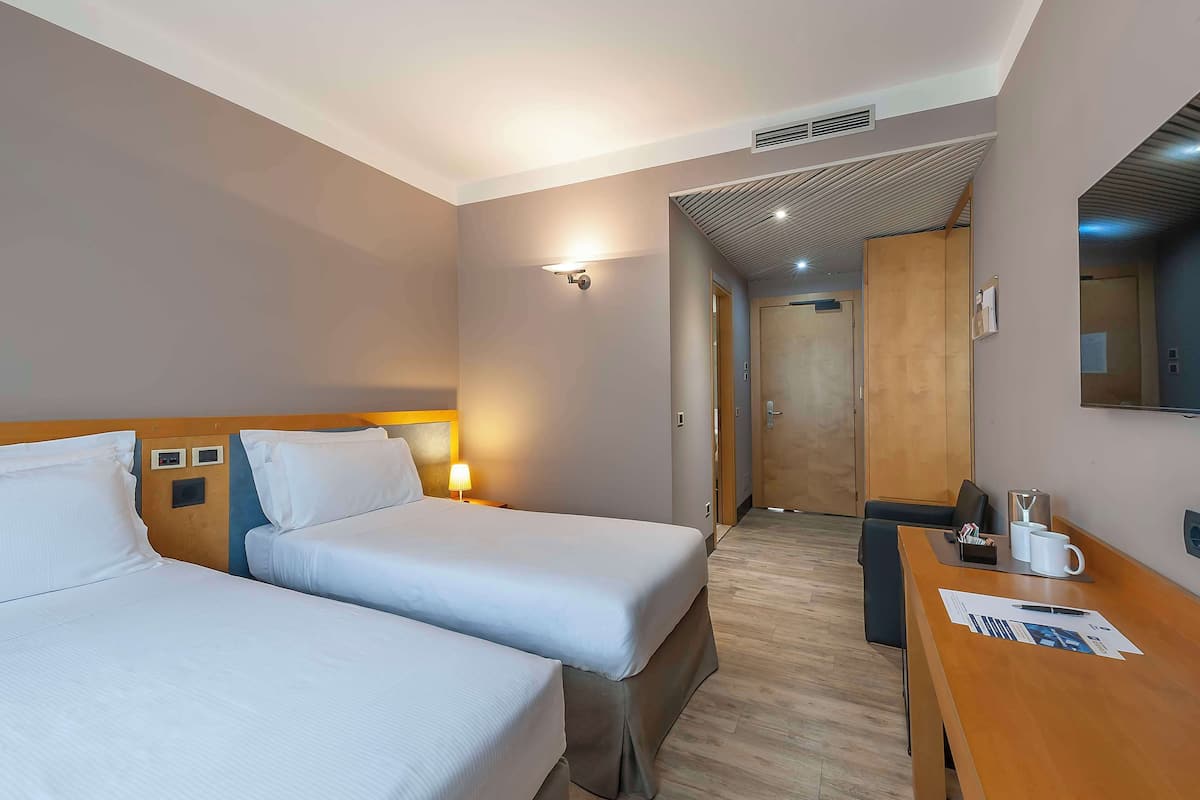 Une chambre d’hôtel avec deux lits, un bureau avec une tasse à café et un miroir au mur.
