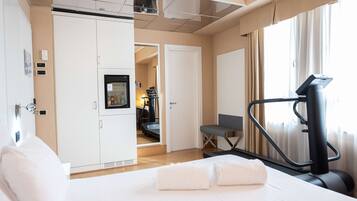 A hotel room with a bed, exercise equipment, a desk, and a view of the hallway.