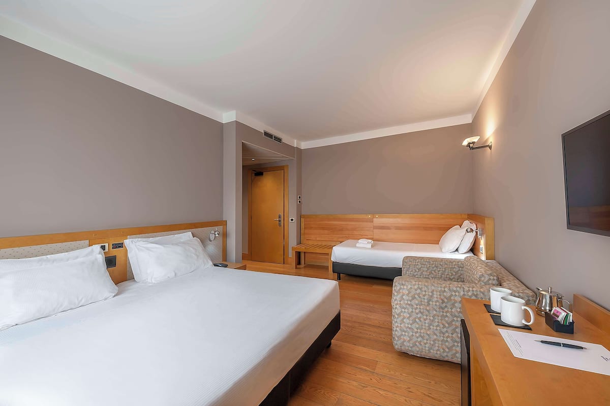 Une chambre d’hôtel avec deux lits, un bureau avec une chaise et un téléviseur fixé au mur.