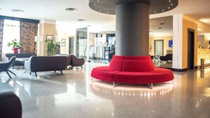 Un hall d’entrée moderne avec un espace de détente central aux sièges rouges, une grande colonne et une cloison en verre.