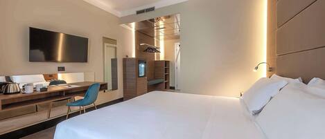 Una habitación de hotel moderna con una cama grande, un escritorio con silla, un televisor de pantalla plana y un vestidor.