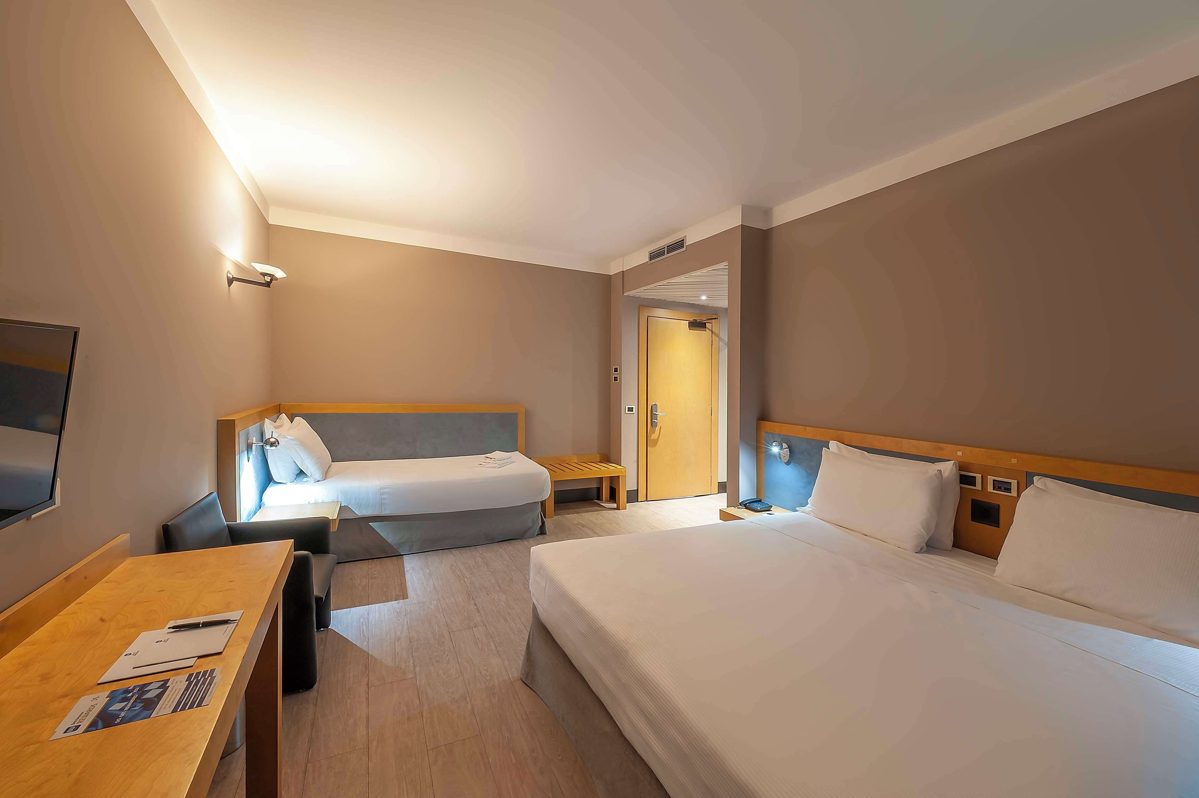 Habitación de hotel con dos camas, un escritorio, un televisor y una puerta que da a otra habitación.