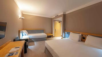Habitación de hotel con dos camas, un escritorio, un televisor y una puerta que da a otra habitación.