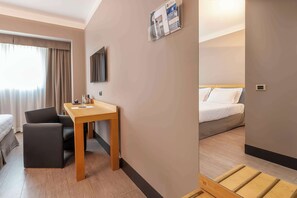 Une chambre d’hôtel avec un bureau en bois, une chaise, un lit et une grande fenêtre avec des rideaux.