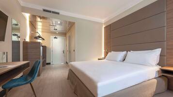 Habitación de hotel moderna con una cama grande, un escritorio y una silla. Hay un espejo en la pared y una puerta que da a otra habitación.