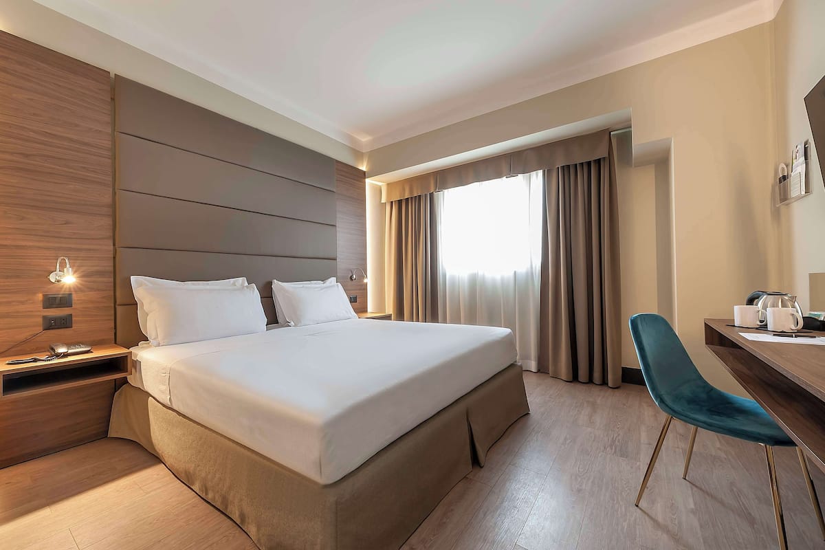 Une chambre d’hôtel moderne avec un grand lit, un bureau avec une chaise et une fenêtre avec des rideaux.