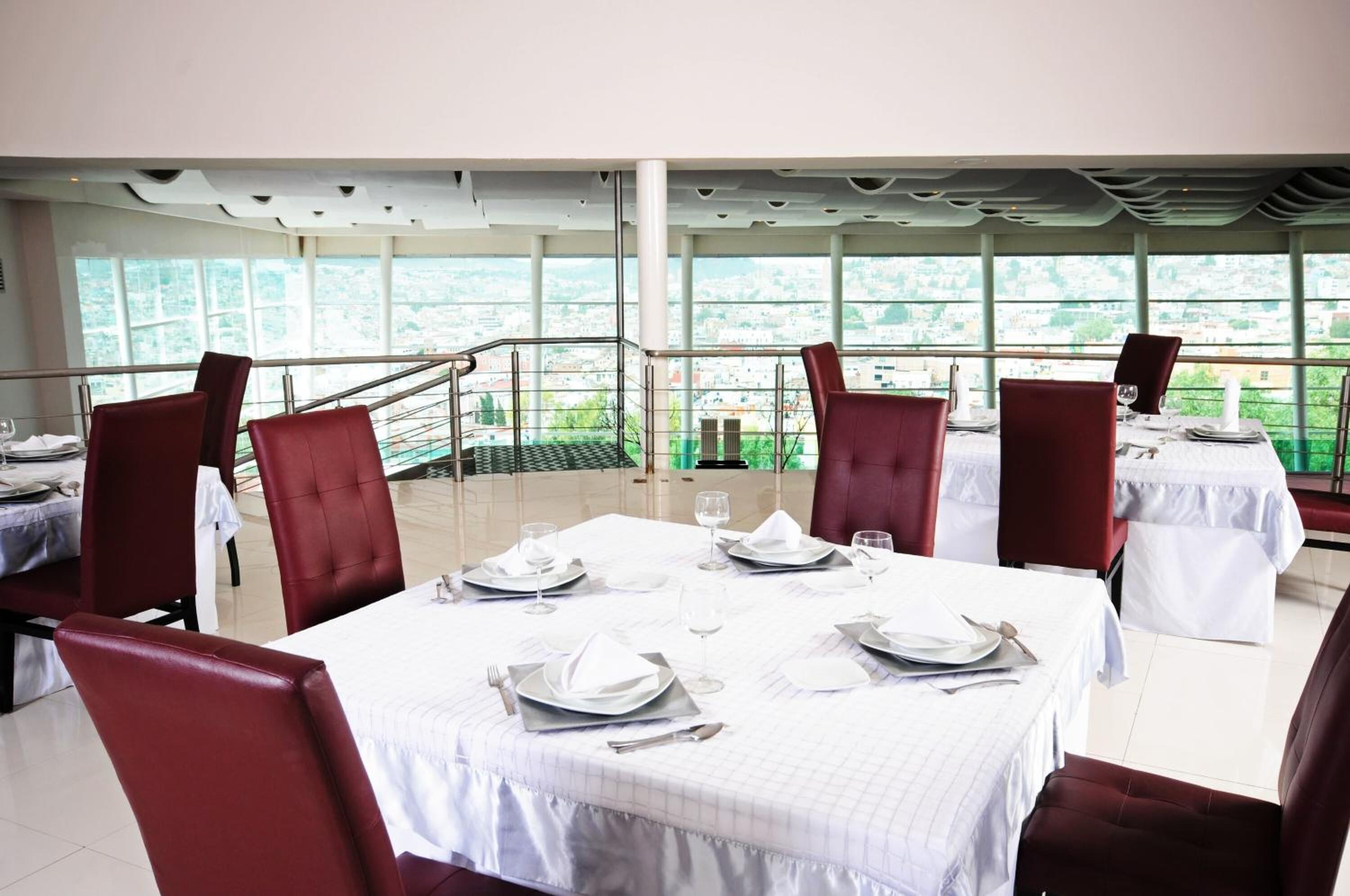 A restaurant with tables set for dining, large windows, and a view of the city.