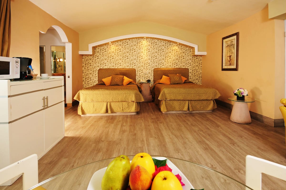 Habitación de hotel con dos camas, una mesita con fruta, un microondas y una silla.