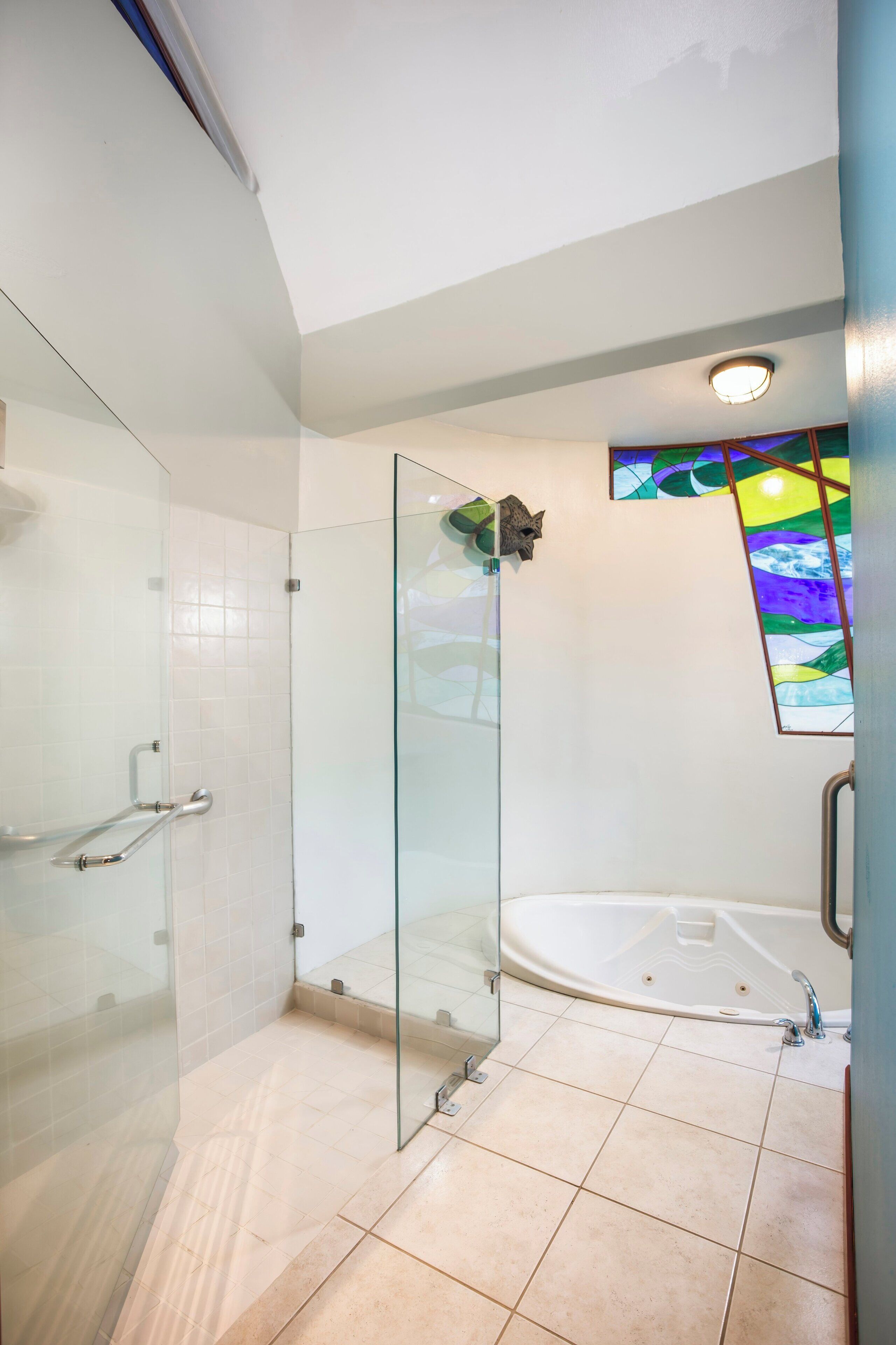 Een moderne badkamer met een glazen douchecabine, een vrijstaand bad en een glas-in-loodraam.