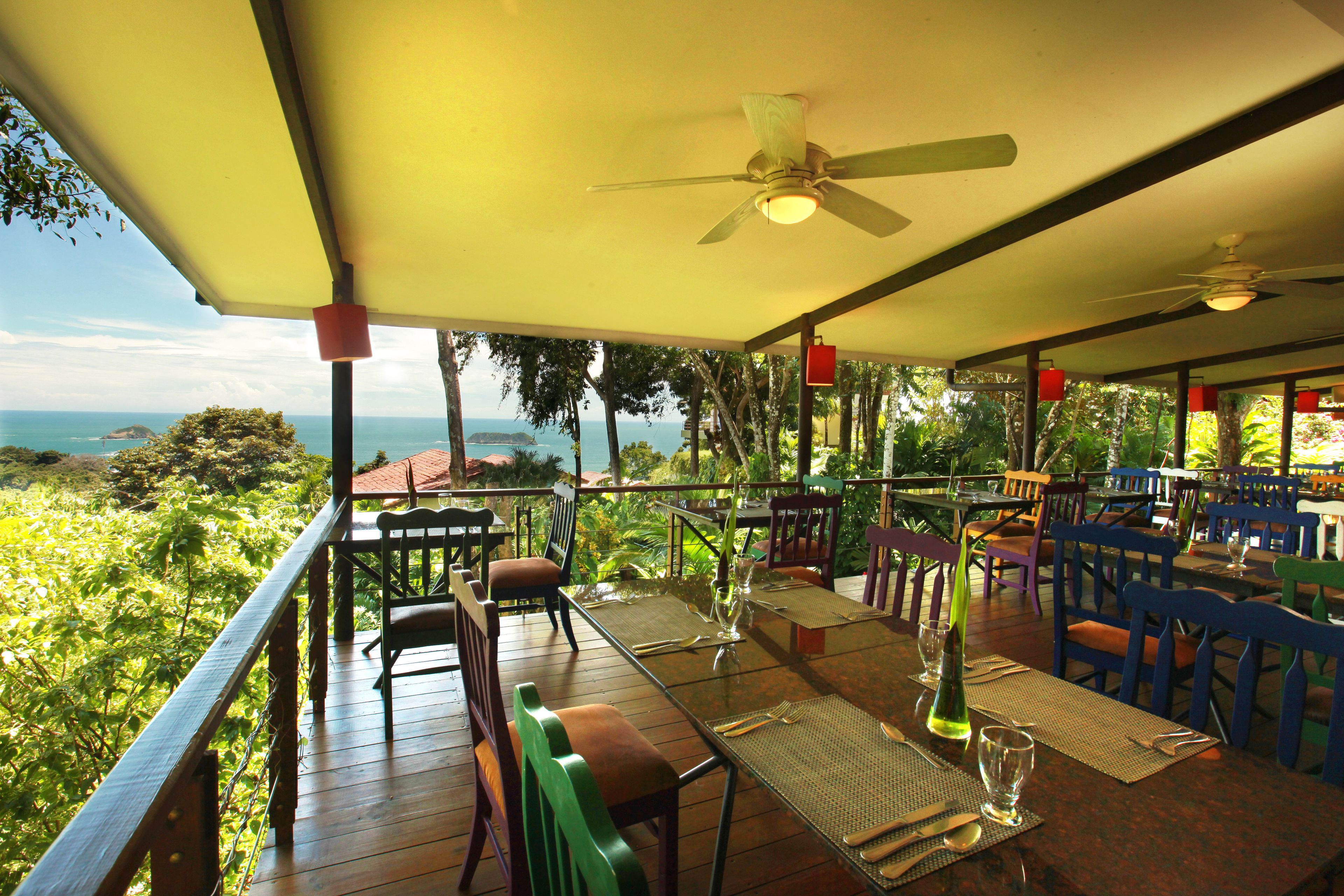 An outdoor dining area with tables and chairs, a view of the ocean, and ceiling fans.