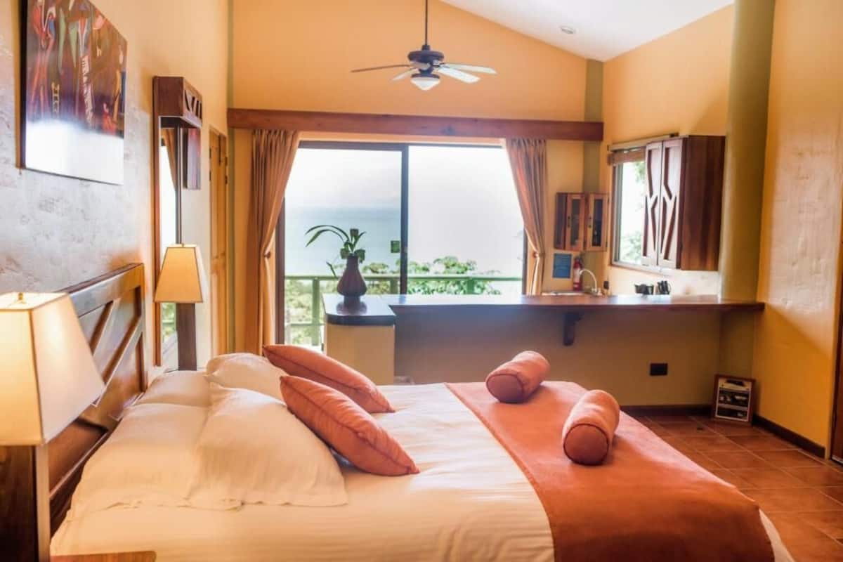 Une chambre d’hôtel avec un lit, un ventilateur de plafond, une fenêtre avec des rideaux et une vue sur l’extérieur.