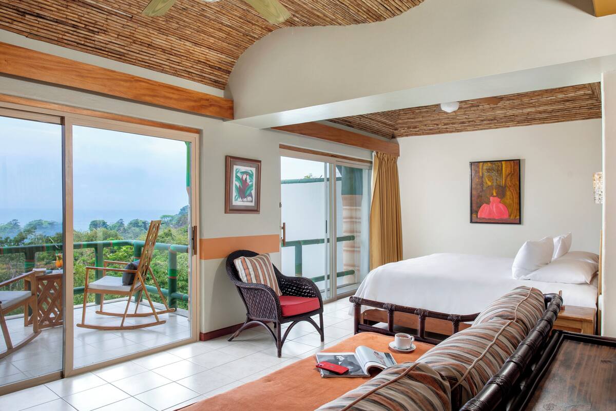 Une chambre d’hôtel dotée d’un grand lit, d’un canapé, d’un fauteuil à bascule, d’une table à manger et d’un balcon offrant une vue sur le paysage.
