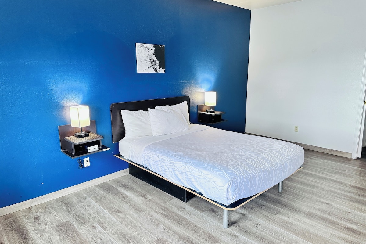 A hotel room with a bed, two bedside tables with lamps, a wall art piece, and a wooden floor.