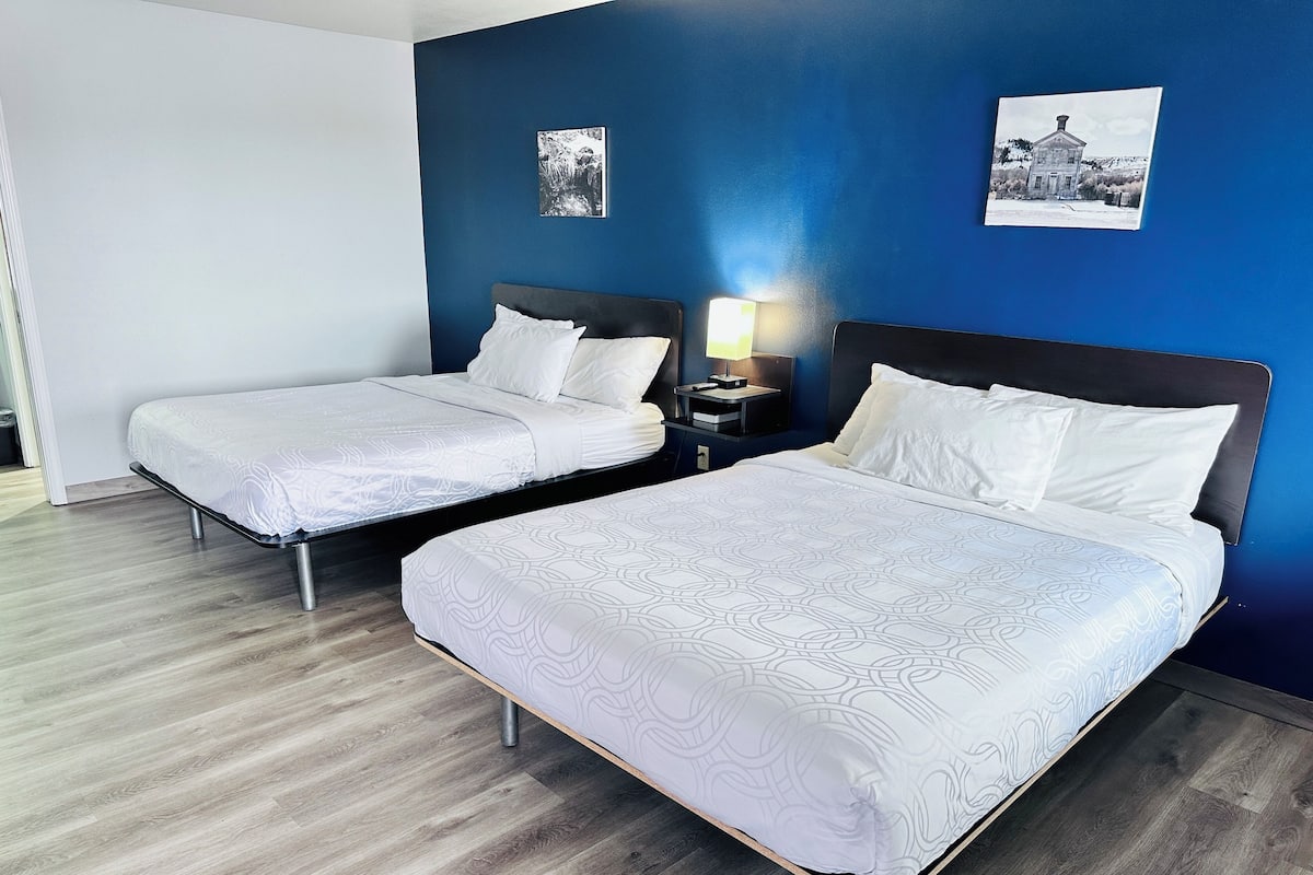 A hotel room with two single beds, a nightstand with a lamp, and a wall-mounted picture.
