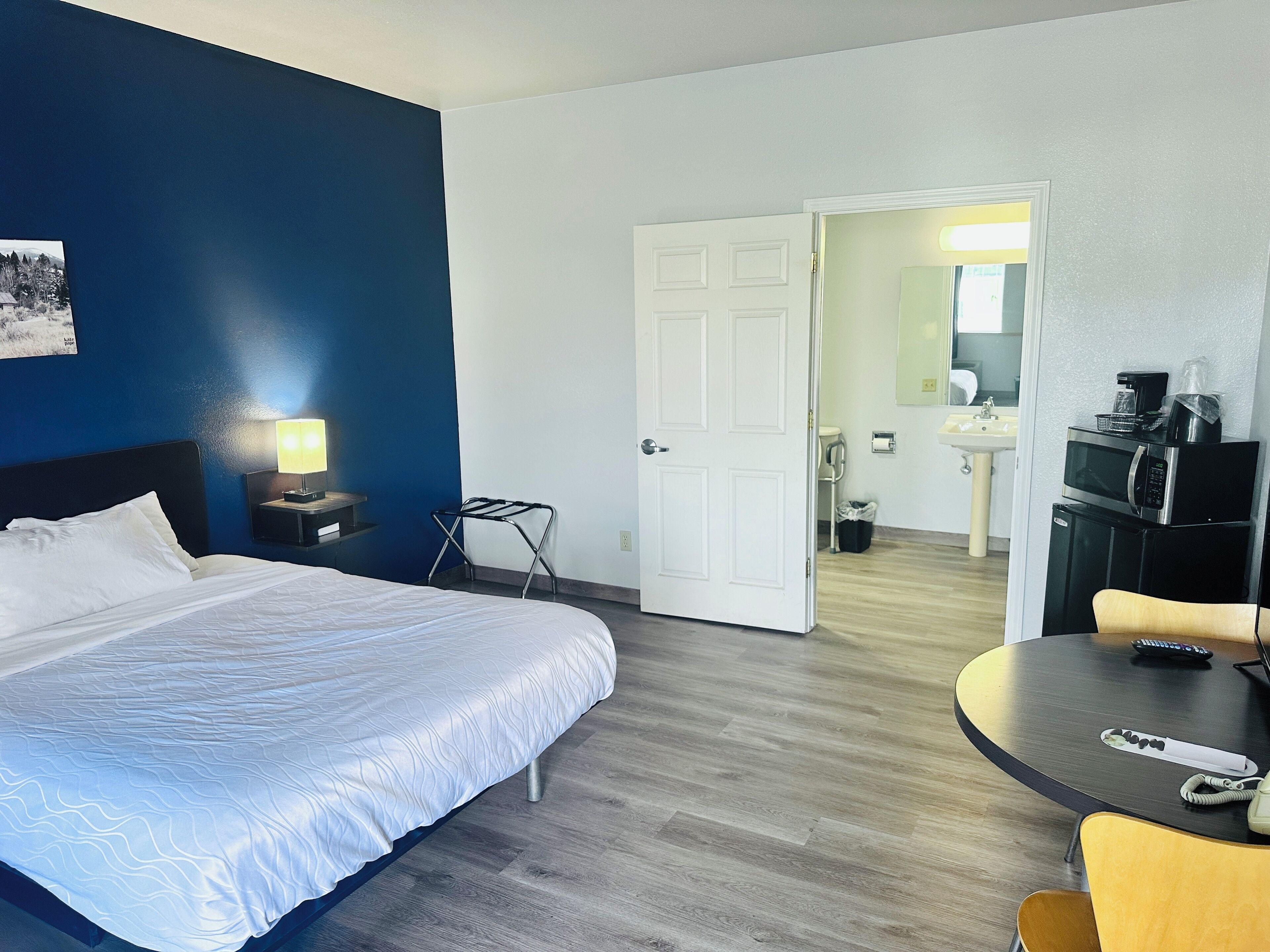 A hotel room with a bed, a desk with a chair, a microwave, and a sink.