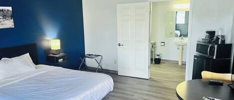 A hotel room with a bed, a desk with a chair, a microwave, and a sink.