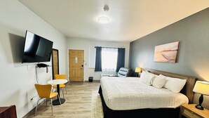 Een hotelkamer met een bed, een bureau met stoel, een televisie, een raam met gordijnen en een schilderij aan de muur.