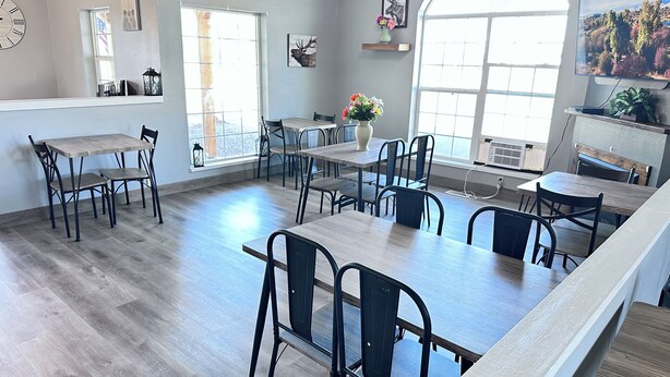Een ruime eethoek met meerdere tafels en stoelen, grote ramen met natuurlijk licht en een moderne kroonluchter.