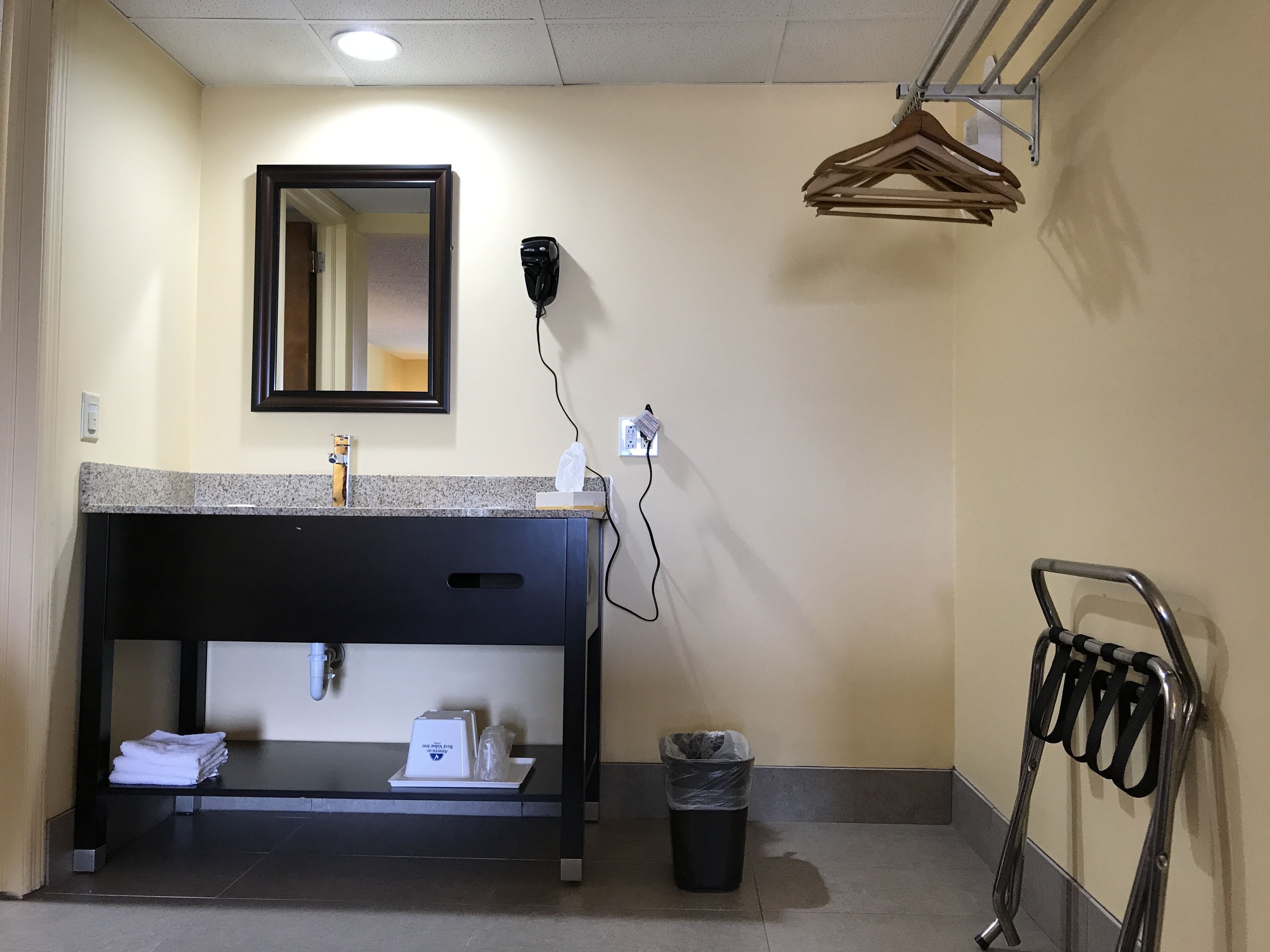 Un baño con lavamanos, espejo, dispensador de toallas y cubo de basura.