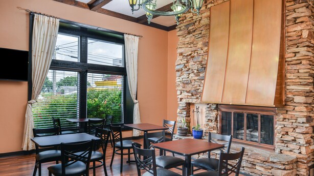 A restaurant with wooden tables and chairs, a stone wall, and a large window with curtains.