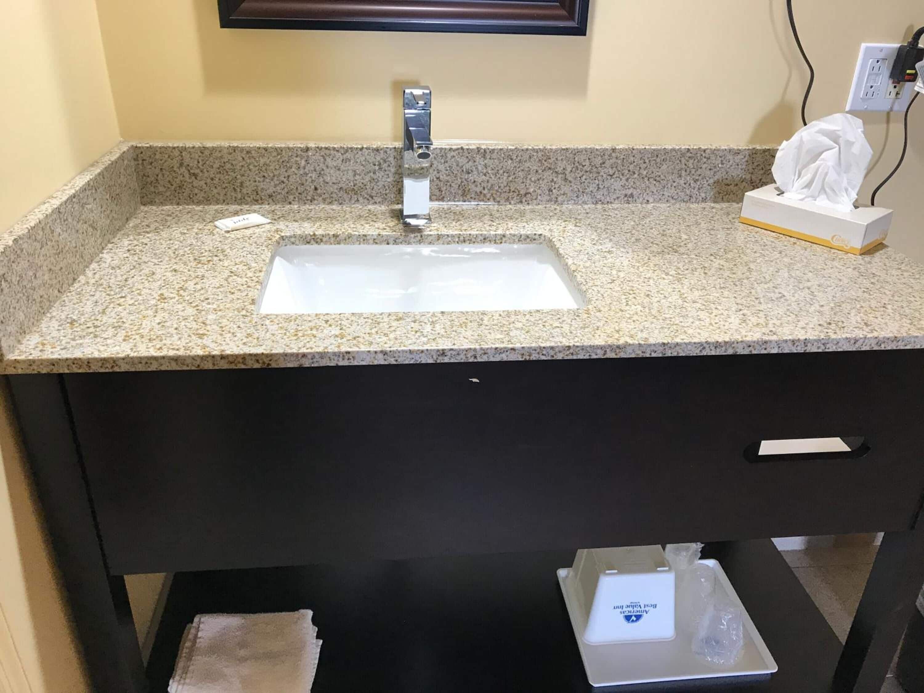 Un baño con encimera de granito, un lavamanos blanco, un espejo y una caja de pañuelos.