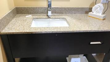 Un baño con encimera de granito, un lavamanos blanco, un espejo y una caja de pañuelos.