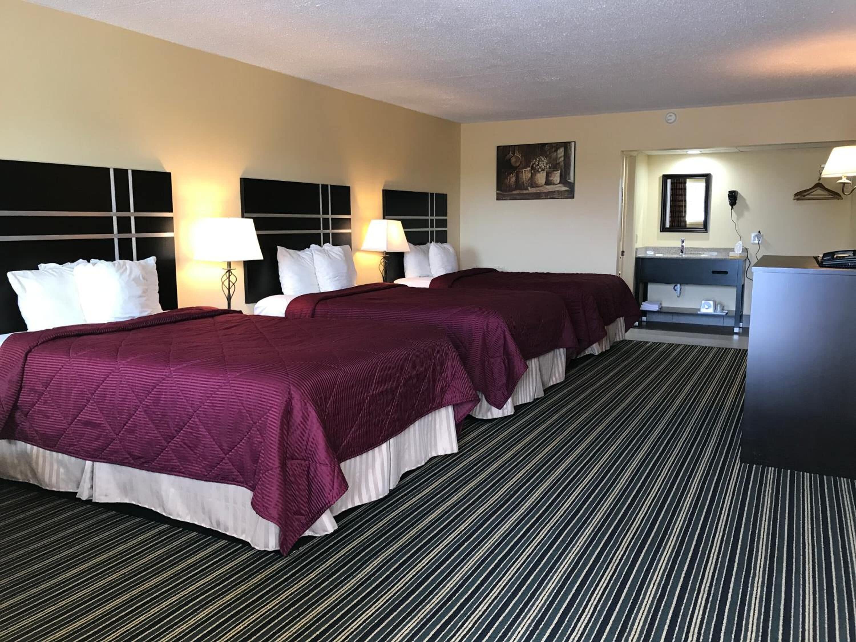 Habitación de hotel con dos camas, un escritorio, un aparador y un cuadro en la pared.