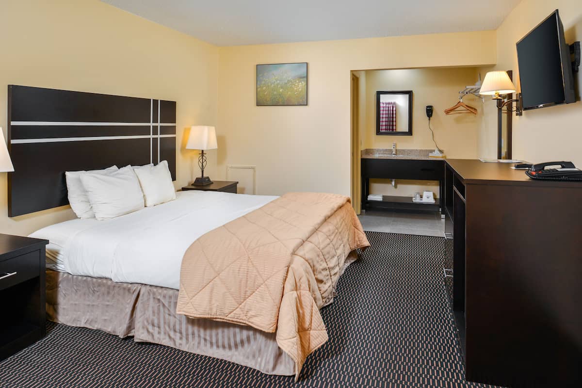 A hotel room with a bed, bedside table, lamp, TV, and a desk with a chair.
