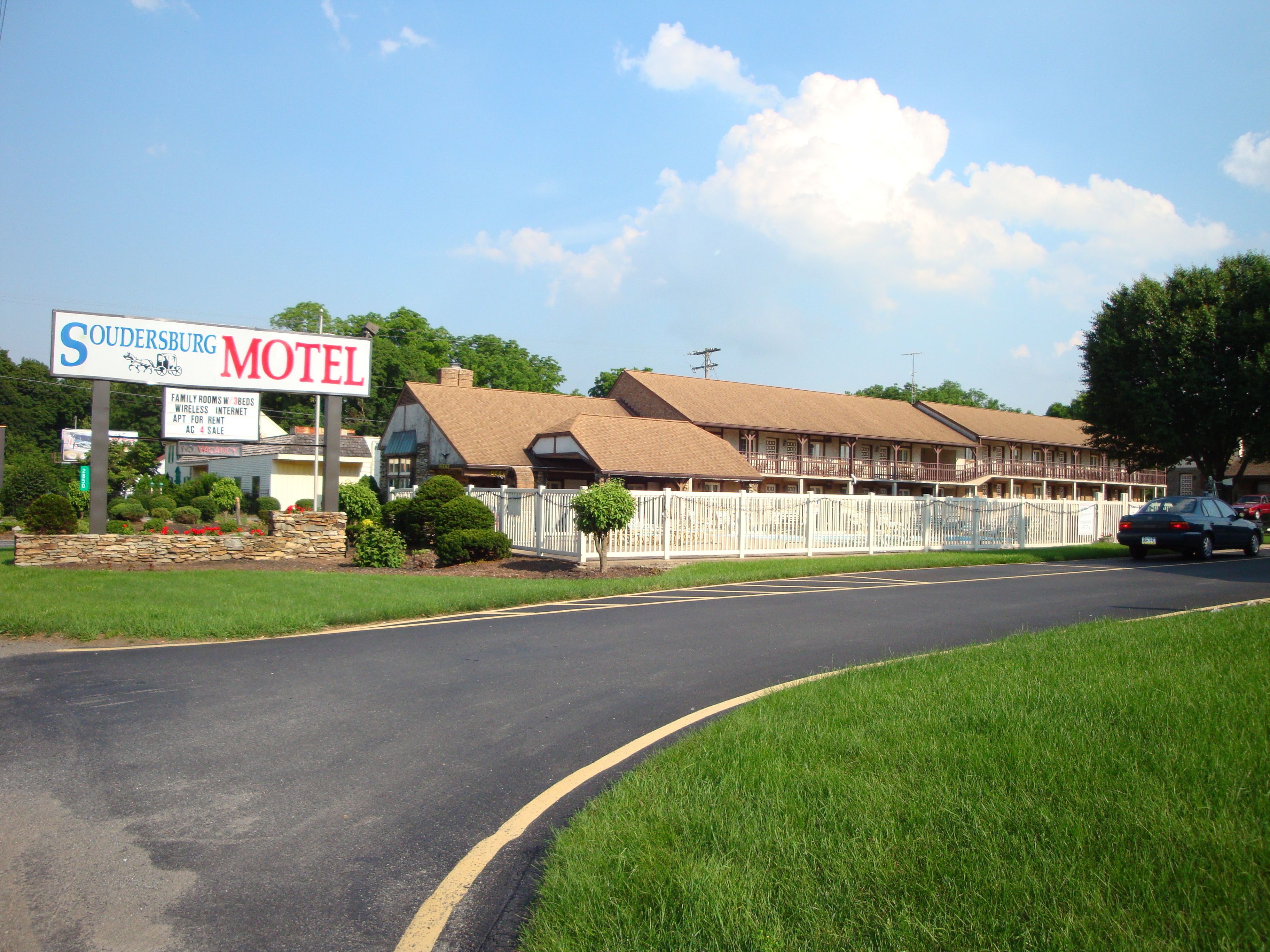 A motel with a signboard, a fenced parking area, and a road curving ahead.