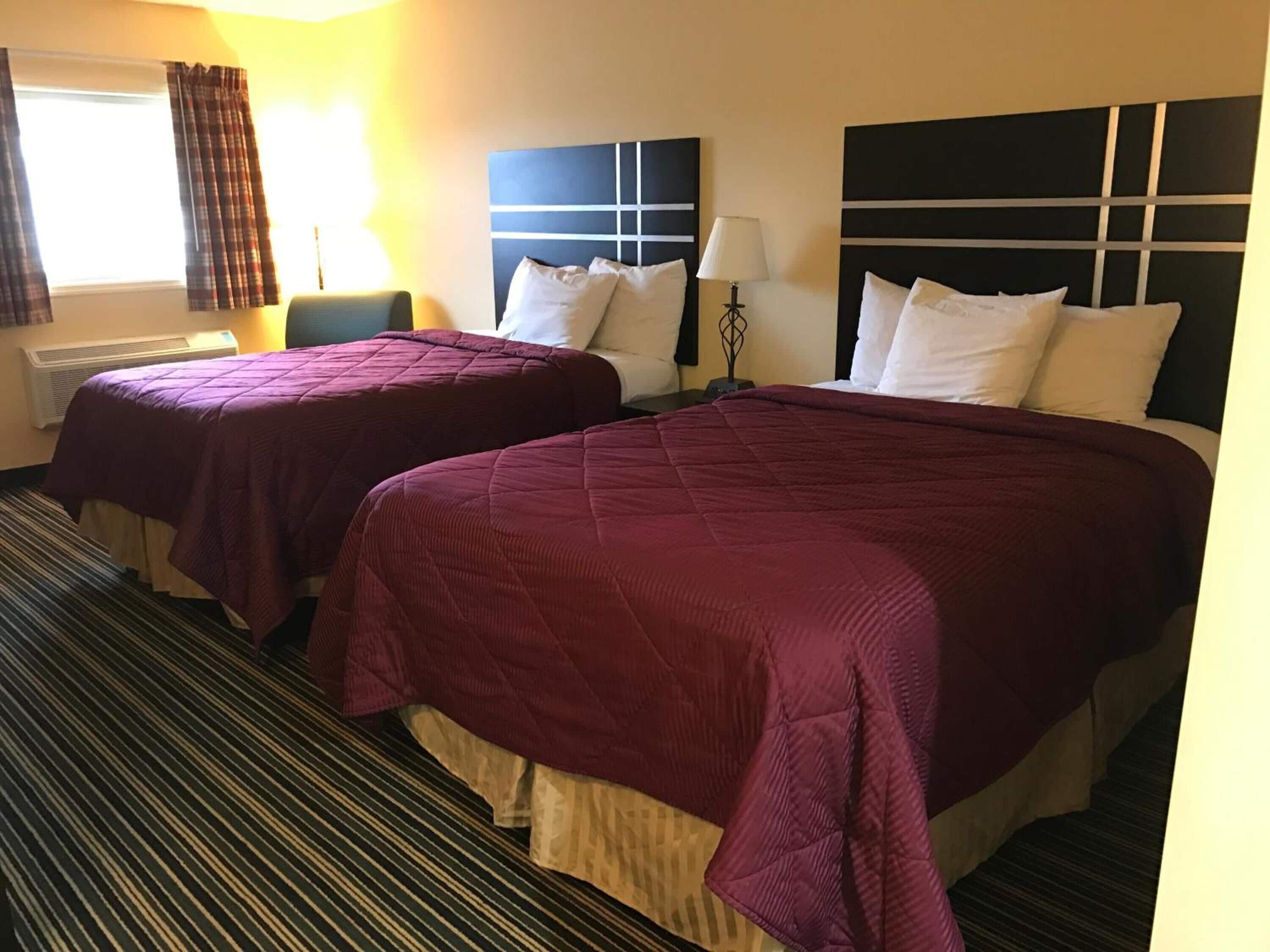 Habitación de hotel con dos camas, cada una con cabecero, una ventana con cortinas, una lámpara y un radiador.