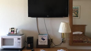 A hotel room with a flat-screen TV mounted on the wall, a microwave on the counter, a coffee maker, a lamp, and a bed with a floral bedspread. - Fabens Inn Motel (Fabens)
